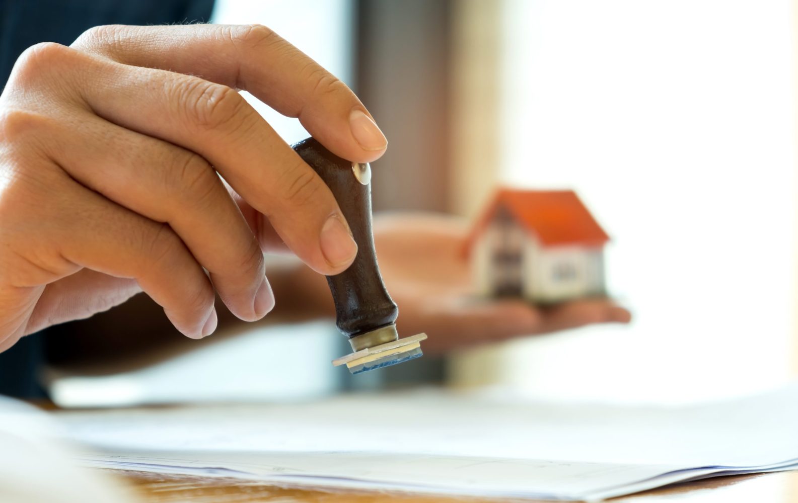 Close-up rubber stamp and model house in hand,Concept image of home mortgage business.